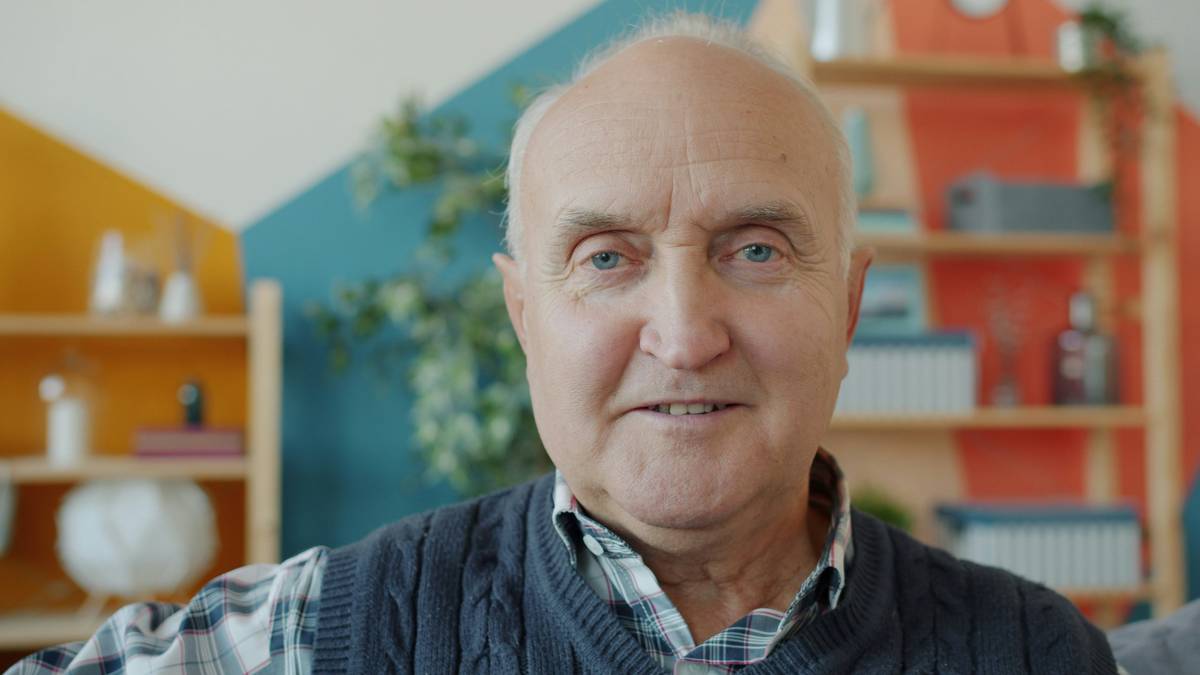Close-up portrait of good-looking retired gray-haired man looking at camera at home with light smile. Positive emotions and retirement concept.