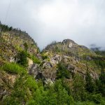 Rugged mountainside with green trees under a cloudy sky.